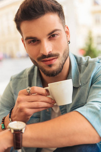 微笑休闲男子在市中心的桌子旁喝咖啡休息时拿着杯子的肖像