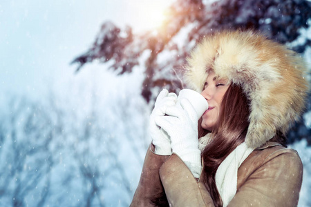 风平浪静心满意足的女人在白雪覆盖的树林中尽情地喝着热咖啡，在寒冷的晴天在公园里散步，享受寒假