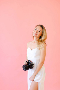 年轻的微笑的女摄影师与照相机在粉红色的单声道背景