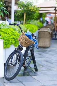 带着篮子的自行车停在咖啡馆旁边的街道上。 篮子里有一件牛仔夹克，接下来是相机的三脚架。