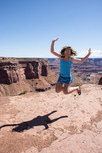 在一个阳光明媚的日子里，成年女性在犹他州峡谷国家公园的一个风景优美的俯瞰处跳跃和微笑。 自由的概念幸福的个人旅行