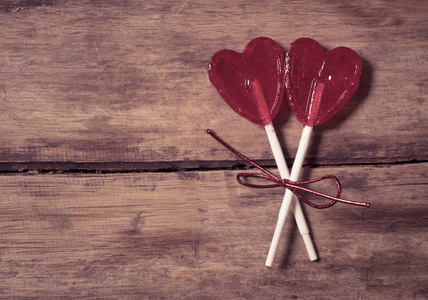 两个可爱的红色心形棒棒糖在乡村木桌上和美丽的浪漫心情，光和模糊的背景，作为隐喻的爱在一起和情人节问候汽车设计理念。
