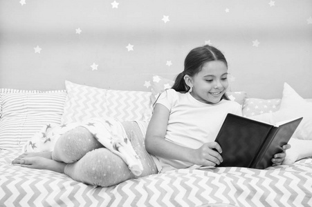 女孩躺在床上看书。孩子准备上床睡觉。在舒适的卧室愉快的时间。小女孩长头发可爱的睡衣放松和看书。满意与幸福的结束。她喜欢关于爱的亲