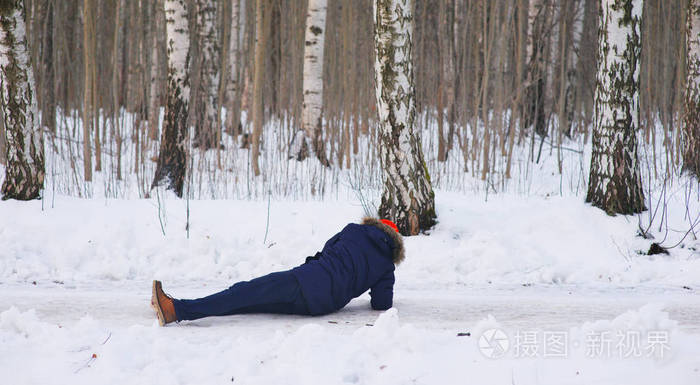 穿着时髦衣服的年轻人在桦树林散步时在滑滑的道路上滑倒那家伙摔倒了