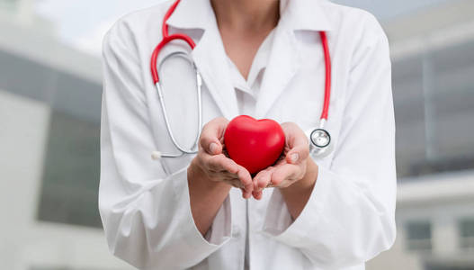 医生在医院办公室捧着一颗红色的心。 医疗保健和医生服务理念。