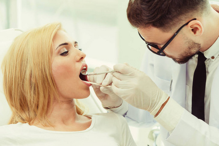 年轻英俊的牙医在牙科诊所里坐在牙科椅上检查快乐妇女病人的牙齿。 牙科护理概念。