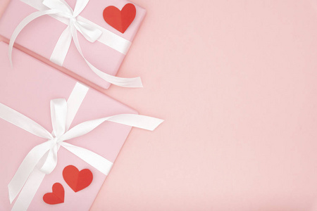 情人节或妇女的一天粉红色的礼物与白色的蝴蝶结丝带装饰与红色的小心脏在珊瑚纸的背景。概念装饰爱的一天或生日。平躺着。复制空间