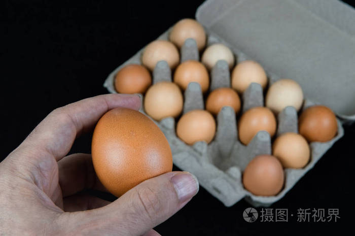 男人手里拿着一个鸡蛋从黑色毛毡背景上的纸板蛋盒里拿出来