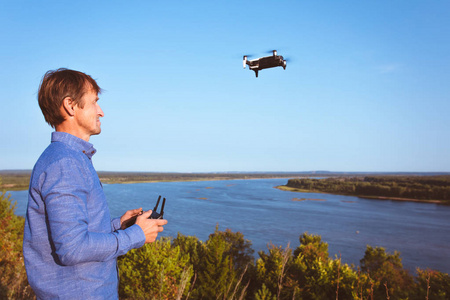一个人发射四方直升机。 在阳光明媚的一天，无人机飞过河流和森林