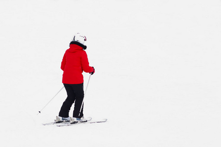 穿着红色西装的女滑雪者在雪山的背景下滑下。 冬季运动的现代体育设备。 滑雪场。 露天的体育活动。 面对审判。