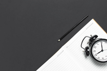 闹钟桌面平躺黑色闹钟,清洁打开笔记本日记,铅笔在灰色深色背景顶视