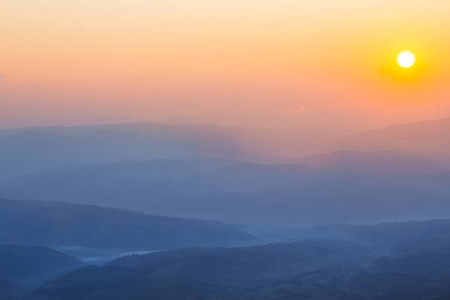 黎明时分,山峦在蓝雾中,日出在山链上照片