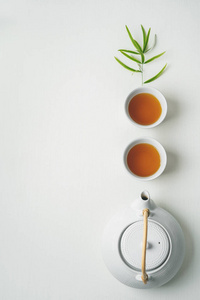 白色的茶杯和茶壶，白色的背景上环绕着绿色的竹叶