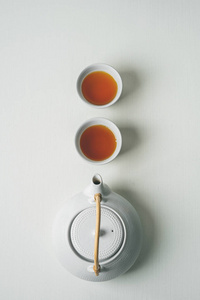 亚洲极简主义的茶概念，两杯白茶和茶壶从上面看，空间为白色织物背景上的文字。