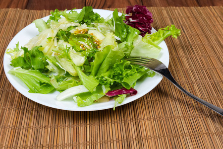 绿红生菜品种的叶沙拉，配芥末沙拉酱，餐盘上有叉子，夹在竹桌垫上