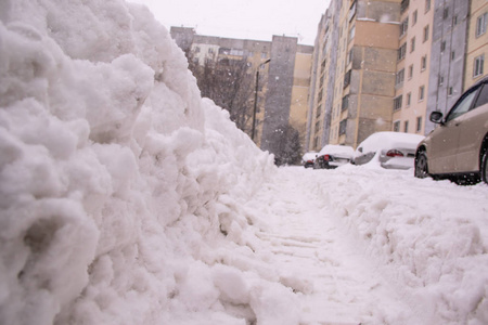 在大雪的背景下，从汽车上下来的小径踏在道路上，覆盖着多层的建筑物和汽车