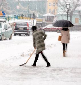 女人在城市街道上铲冬天的雪。 故意动作模糊