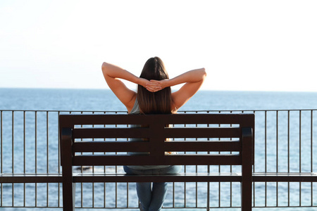 一位坐在长凳上沉思大海的妇女在海滩上放松的后景肖像