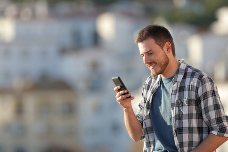 幸福的男人在日落时分在镇上查看智能手机短信