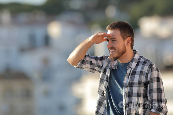 快乐的男人用手在额头上侦察在城里向前看