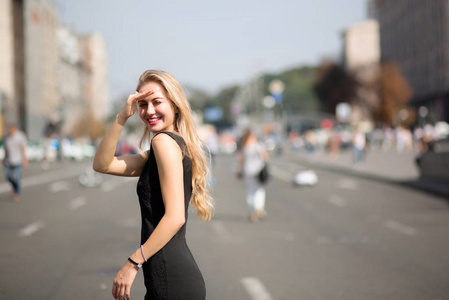 情绪激动的金发女人，长发，穿着黑色连衣裙，走在阳光明媚的街道上。 文本空间