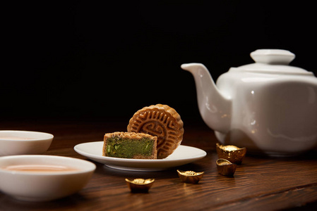 传统美味的中国月饼茶壶和金锭在木桌上隔离在黑色上