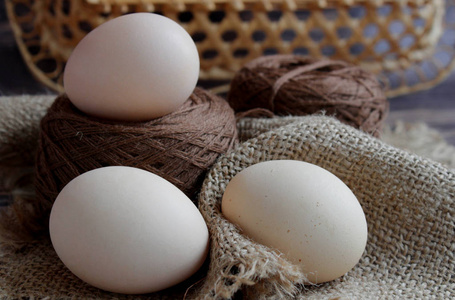 三个鸡蛋和棕色的线躺在米色的餐巾纸上，背景很黑。 木质柳条背景后面