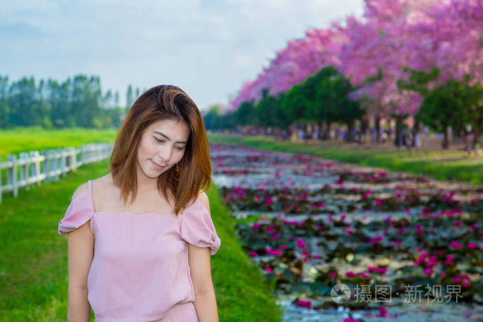 一位年轻的亚洲妇女，带着盛开的樱花树走在花园里