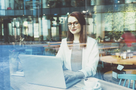 在现代城市咖啡馆里，年轻女性在笔记本电脑上工作的近景
