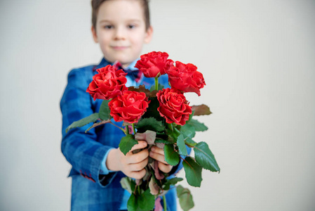 可爱的小男孩，穿着西装，手里拿着一束红色玫瑰，背景轻盈，情人节的概念