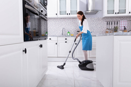 清洁厨房地板和真空地板的年轻女清洁工