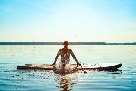 快乐的女人放松在冲浪板上，享受生活。 站起来划桨登机，令人敬畏的积极户外娱乐。 背光。