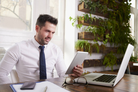 商人穿着衬衫和领带，使用数字平板电脑，而坐在办公桌和工作的新项目。