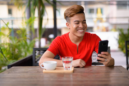 快乐的年轻亚洲人在户外咖啡店使用电话