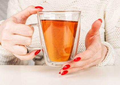 雌性手拿着一杯透明的热茶。美丽的红色指甲