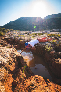 精疲力竭的冒险家在阳光明媚的一天从海滨岩石的缝隙中喝水在冒险旅行时生存。背光。