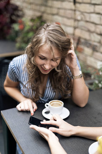 当代女性朋友在咖啡馆的餐桌上享受咖啡，同时分享智能手机和微笑