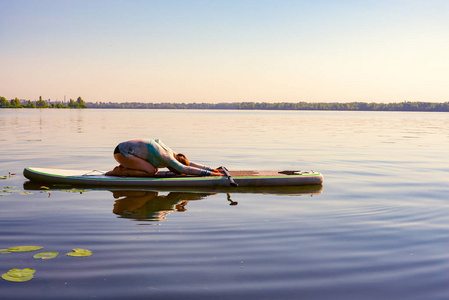 女人在一条大河上的SUP板上练习瑜伽。站起来划桨登机在大自然中令人敬畏的积极训练。