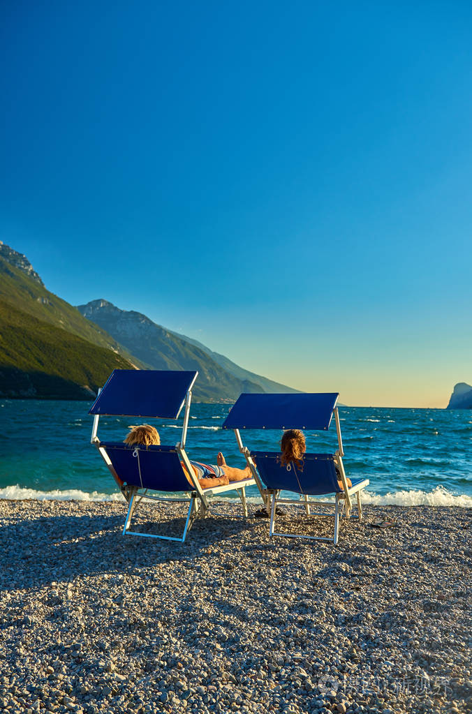 人们坐在沙滩上的躺椅上欣赏夏天的加德纳湖欣赏群山环绕的美丽的
