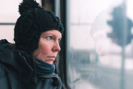 在寒冷的冬日，公共汽车上悲伤的女人透过窗户望着街道