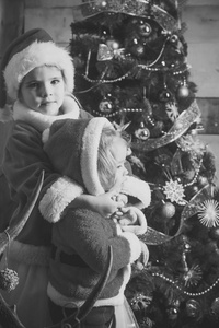 新年小女孩和男孩的幸福。 圣诞老人圣诞树上的孩子。 圣诞晚会庆祝童年寒假和假期。 圣诞快乐的孩子戴着红帽子。