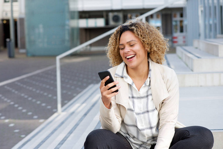 幸福的年轻非洲裔美国妇女在外面看手机的画像