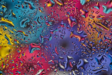 明亮的彩色背景模糊和扭曲的水滴在玻璃表面。