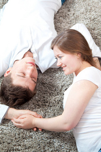 幸福的年轻情侣躺在灰色蓬松的地毯上