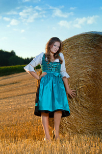 美丽的年轻女子穿着蓝色的衣服在麦田的干草堆旁摆姿势