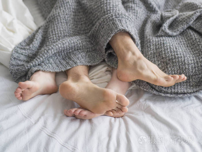 两对夫妇睡在灰色毯子下的床上的脚