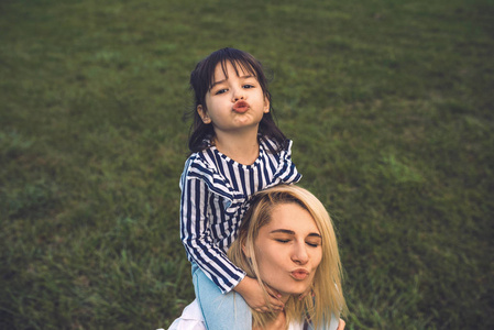 美丽的女人在户外绿草上和她可爱的小女孩玩和吹吻的形象。 爱美丽的母女在公园里度过时光。 妈妈和孩子玩得开心