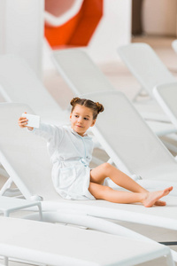 可爱的孩子穿着浴袍，躺在躺椅上自拍