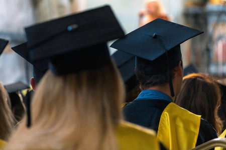 在大学毕业典礼上，学生们穿着长袍和帽子坐在室内等待毕业典礼
