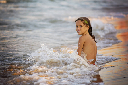 海边被别墅坐在海边的小女孩被海浪覆盖着.照片
